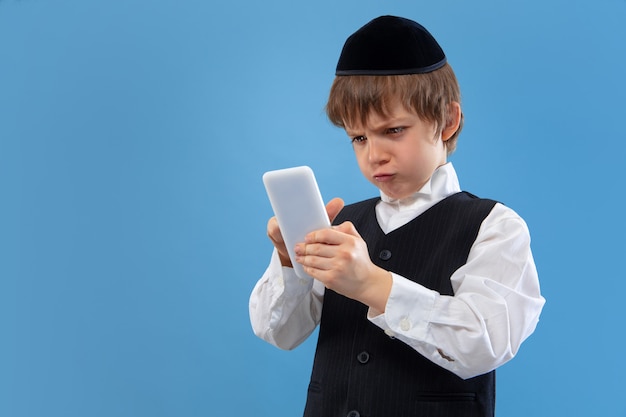 Портрет молодого ортодоксального еврейского мальчика изолированного на голубой студии