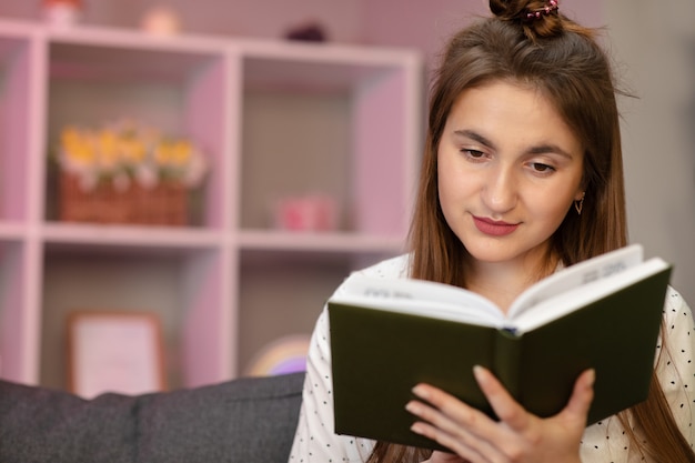 책을 읽고 젊은 학생의 초상화입니다. 집에서 침대에서 책을 읽고 아름다운 젊은 갈색 머리 여자