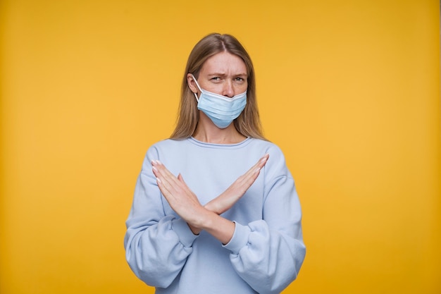 Бесплатное фото Портрет молодой женщины в медицинской маске, показывающей руками знак отказа
