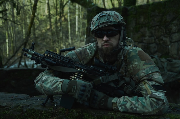 森の中で機関銃を備えたプロの機器でエアガンプレーヤーの肖像画。戦争で武器を持った兵士