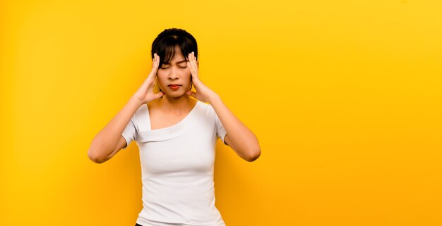 Портрет азиатской девушки руки касаясь висков, чувствуя стресс, головную боль. головокружение из-за стресса на желтом фоне Premium Фотографии