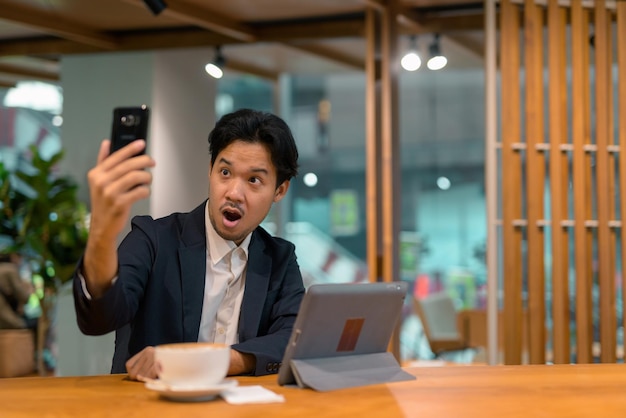 디지털 태블릿 컴퓨터와 휴대 전화를 사용하여 커피숍에서 아시아 사업가의 초상화
