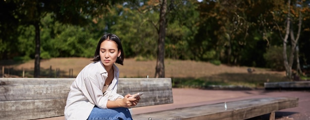 무료 사진 스마트폰과 함께 앉아 있는 아시아 소녀의 초상화 슬프고 우울하고 좌절한 모습으로 기다리고 있습니다.