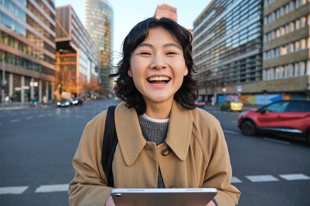 無料写真 アジアの女子学生の肖像画は、にぎやかな通りに車で市内中心部に立ち、デジタル タブレットを保持しています。