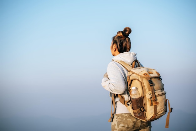 Бесплатное фото Портрет азиатской молодой туристки, прогуливающейся по вершине горы и смотрящей на красивый пейзаж с копировальным пространством.