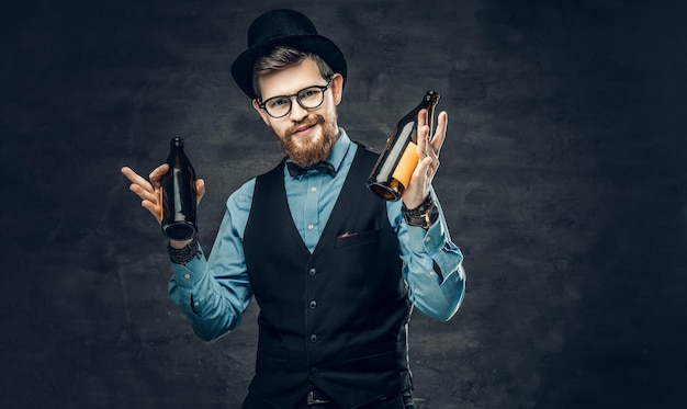 Бесплатное фото Портрет бородатого мужчины-хипстера, одетого в синюю рубашку, элегантный жилет и цилиндр, держит две бутылки крафтового пива и думает о вечеринке.