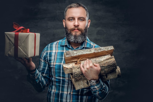 Бесплатное фото Портрет бородатого мужчины средних лет держит дрова и рождественскую подарочную коробку.