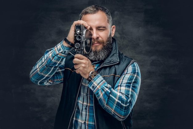 ひげ​を​生やした​中年​男性​の​肖像画​は​、​灰色​の​背景​の​上に​ヴィンテージ​8​mm​ビデオカメラ​を​保持します​。