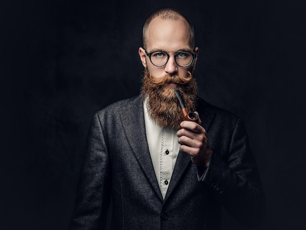 Бесплатное фото Портрет бородатого рыжеволосого английского мужчины курит трубку на сером фоне.