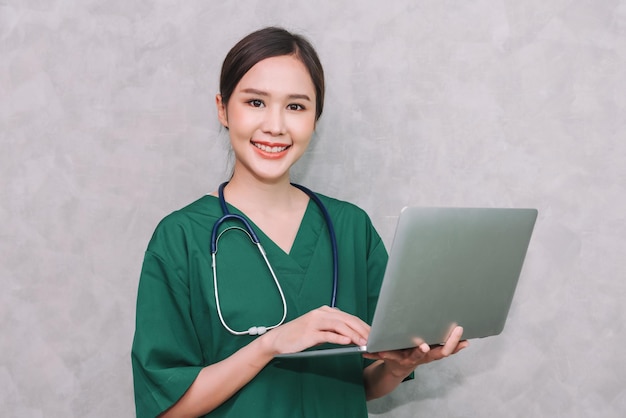 灰色の背景で隔離のラップトップを使用して美しいアジアの女性医師の医療従事者の肖像画
