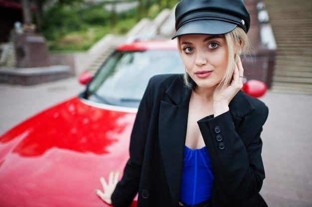 赤い都市の車の近くに明るいメイクで、キャップとすべての黒、青のコルセットで美しい金髪のセクシーなファッションの女性モデルの肖像画。 Premium写真