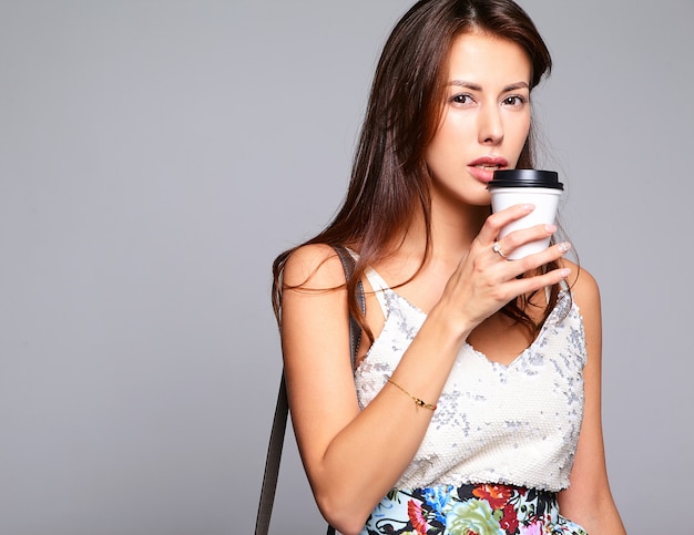 無料写真 グレーに分離された化粧なしでカジュアルな夏服でかわいいブルネット美人モデルの肖像画。新鮮なコーヒーを飲む