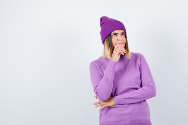 Бесплатное фото Портрет красивой дамы, держащей руку на подбородке в свитере, шапочке и задумчивой вид спереди