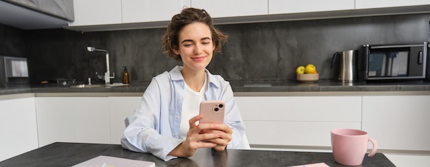 無料写真 スマートフォンアプリの注文を使用してスマートフォンで家に座っている美しい笑顔の女性の肖像画