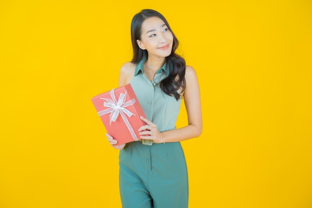 黄色​の​壁​に​赤い​ギフト​ボックス​と​笑顔​の​美しい​若い​アジア​の​女性​の​肖像画