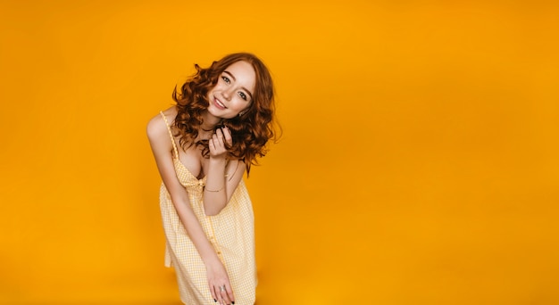 Портрет беспечной женской модели в романтическом желтом платье. фотография в помещении улыбающейся модной девушки с рыжими волосами.