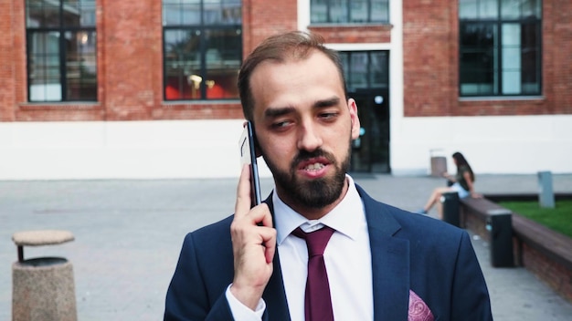 Портрет бизнесмена, держащего смартфон, разговаривает с удаленным менеджером, объясняя стратегию компании, работающую на маркетинговой презентации, стоящей снаружи перед запуском офиса. открытый концепт