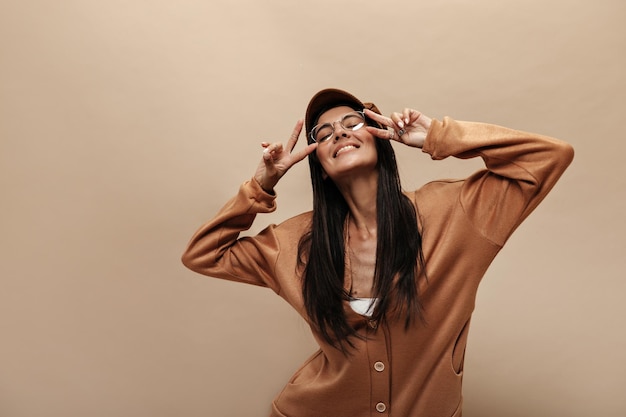 Портрет крутой брюнетки показывает знак мира молодая привлекательная девушка в кашемировом свитере и очках улыбается на изолированном фоне Premium Фотографии