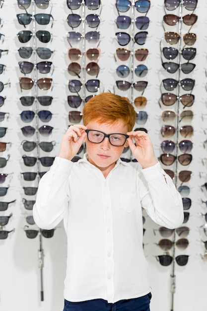 無料写真 眼鏡店で眼鏡店に対して立っている眼鏡を身に着けているかわいい男の子の肖像画