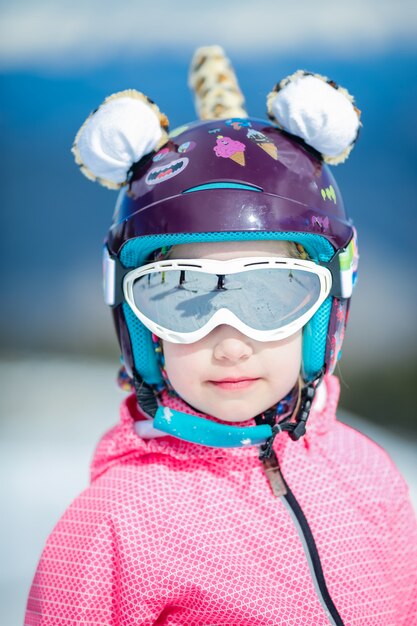 冬のスキーリゾートでヘルメットとゴーグルでかわいい幸せなスキーヤーの少女の肖像画 プレミアム写真