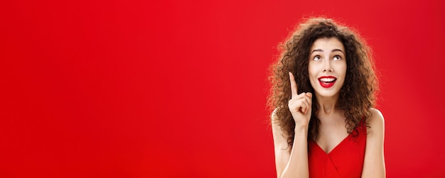 Бесплатное фото Портрет восхищенной очаровательной глупой женщины с кудрявой прической в платье, поднимающей указательный палец в ес