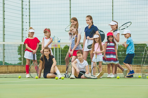 無料写真 屋外コートの緑の芝生に対してテニスラケットを保持しているテニス選手としての女の子のグループの肖像画