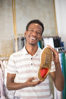 Портрет счастливого афроамериканца, показывающего выбор обуви. красивый мужчина в повседневной одежде, стоящий со спортивной обувью в руке в бутике. обувь и одежда, мода и покупки для мужчин