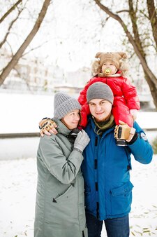 雪の公共公園で屋外でポーズをとって冬のカジュアルな服装で1人の子供と幸せな家族の肖像画
