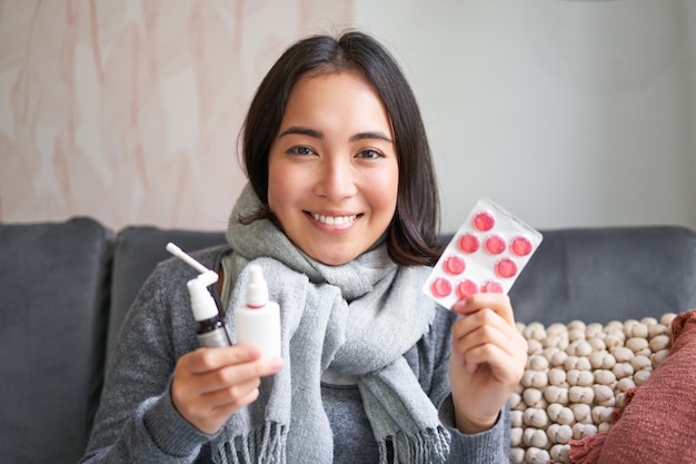 Бесплатное фото Портрет счастливой улыбающейся азиатской девушки, показывающей спрей от боли в горле и лекарства от гриппа или простуды