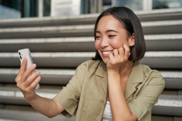 無料写真 幸せな笑顔のアジアの女の子の肖像画は、携帯電話の若い韓国人女性のビデオチャットで自撮りをします