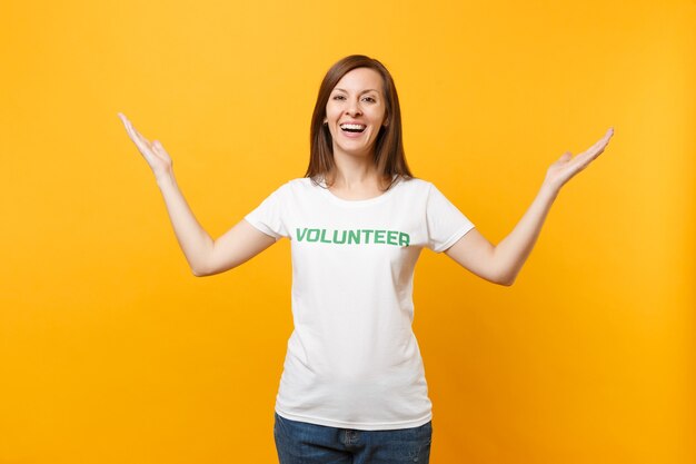 Портрет счастливой улыбающейся довольной женщины в белой футболке с написанным надписью зеленого названия волонтером, изолированным на желтом фоне. добровольная бесплатная помощь, концепция работы благотворительной благодати.