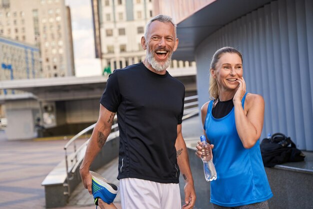 Портрет счастливой спортивной пары среднего возраста, мужчины и женщины в спортивной одежде, улыбаясь, стоя вместе