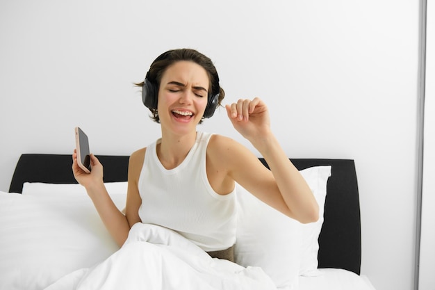 無料写真 ワイヤレスヘッドホンで音楽を聴きながらベッドで踊りながら目覚める幸せな女性の肖像画