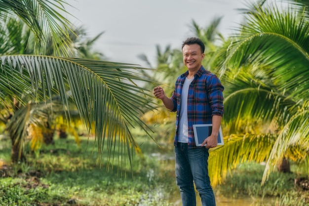 Портрет мужчины средних лет держат планшет стоя и глядя в камеру на открытом воздухе на кокосовой ферме