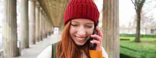無料写真 赤い帽子をかぶった赤毛のヨーロッパの女の子の肖像画は、電話をかけ、街を歩き、友人と話します