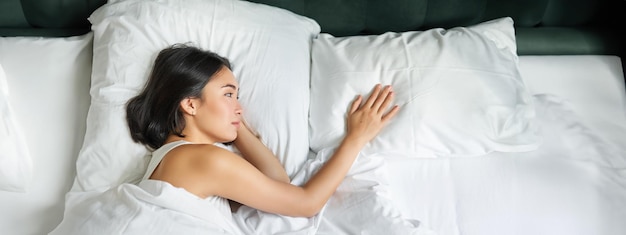 무료 사진 침대에 혼자 누워 빈 베개를 만지고 자신에 대해 생각하는 낭만적인 아시아 여성의 초상화