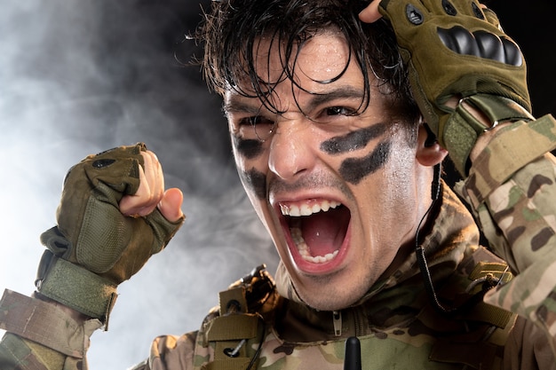 Бесплатное фото Портрет кричащего молодого солдата в камуфляже на темной стене