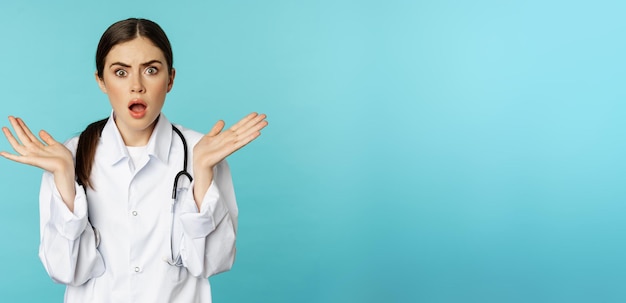 無料写真 ショックを受けた女性医師の肖像画は、青い背景の上に立っている患者を見て心配している白衣の医療従事者を心配しました