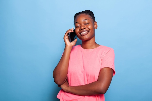 Портрет улыбающегося афроамериканского подростка, разговаривающего по телефону с другом, делящегося советами, стоя в студии на синем фоне. концепция коммуникации. удаленное подключение