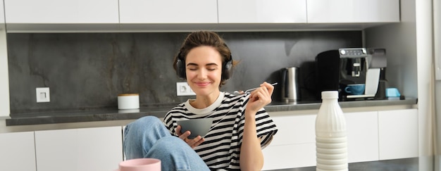 無料写真 笑顔の現代的な女性の肖像画 ⁇ 朝食を食べ ⁇ ミルクでシリアルを食べ ⁇ 音楽を聴いています ⁇