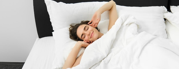 Бесплатное фото Портрет улыбающейся довольной молодой женщины, протягивающей руки, просыпающейся после хорошего ночного сна