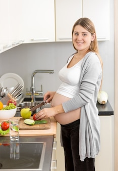 Портрет улыбающейся беременной женщины, готовящей ужин на кухне