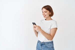Портрет улыбающейся женщины, отправляющей текстовые сообщения и читающей экран телефона счастливая женщина в чате в приложении, стоящем на белом фоне