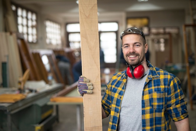 Бесплатное фото Портрет улыбающегося работника столярной мастерской, держащего доску древесного материала