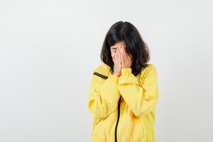 portrait of teen girl holding hands on face in yellow jacket and looking depressed front view