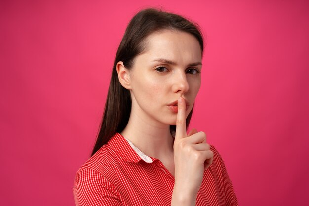 Портрет женщины, держащей палец на губах, чтобы молчать на розовом фоне