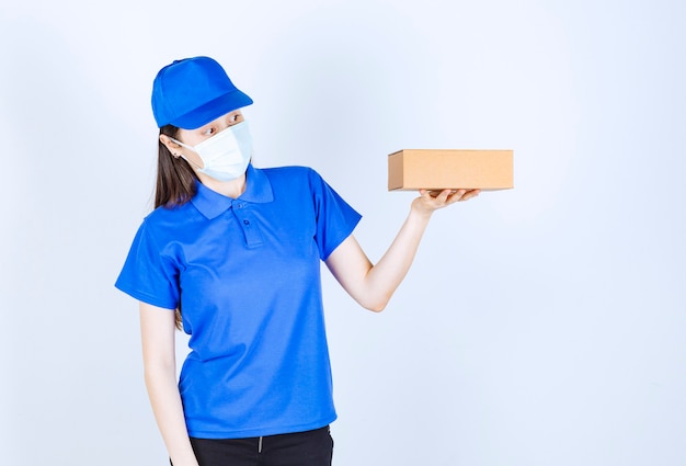 Портрет женщины в форме и медицинской маске, держащей бумажную коробку