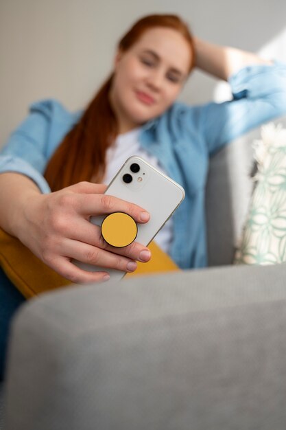 Бесплатное фото Портрет женщины, использующей свой смартфон дома на диване, держась за поп-розетку