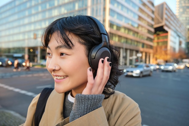 無料写真 若いアジアの女子学生の肖像画は街を歩き、ヘッドフォンで音楽を聴き、携帯電話を使用します