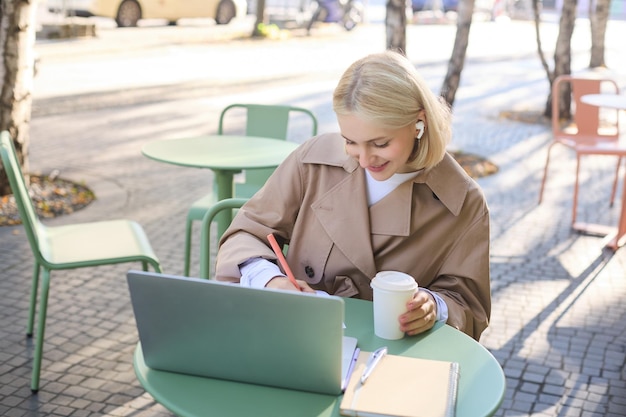 無料写真 ラップトップを使用してワイヤレスヘッドフォンを着用したストリートカフェの若い金 ⁇ の女性学生の肖像画